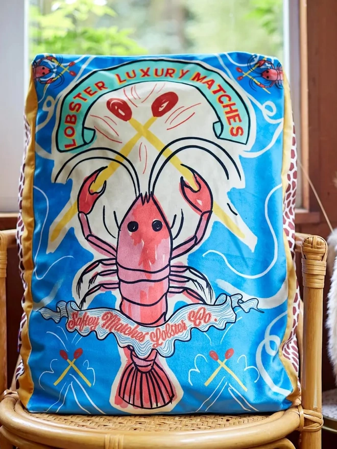 Lobster Matchbox Cushion, a decorated lobster cushion sitting on an arm chair. 