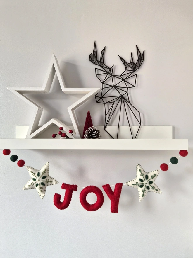 Felt 'Joy' Garland hanging under a white shelf