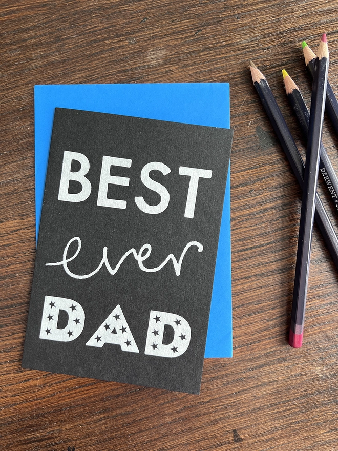 A Mr.PS Best Ever Dad card with a blue envelope on a wooden desk