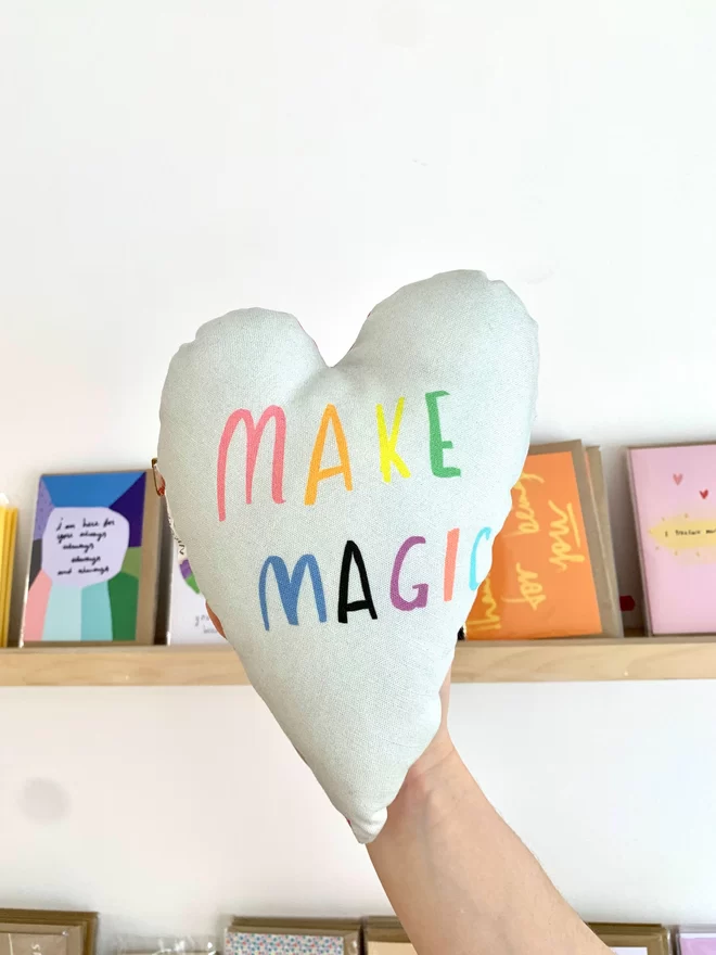 A heart shaped cushion that reads 'MAKE MAGIC'