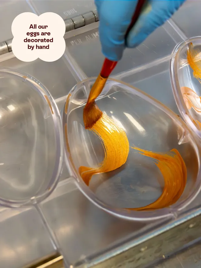 An easter egg mould being painted with gold cocoa butter