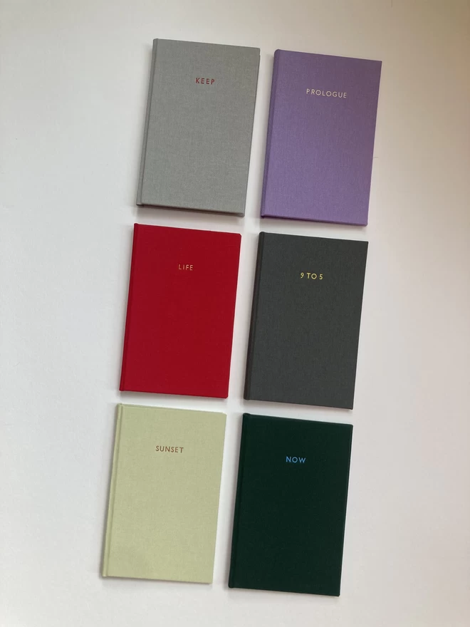 An array of handmade pocket sized notebooks in a variety of book cloth colours with personalised foiled quotes and titles