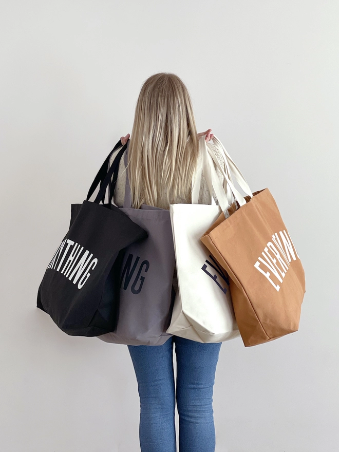 Model carrying four everything oversized tote bags