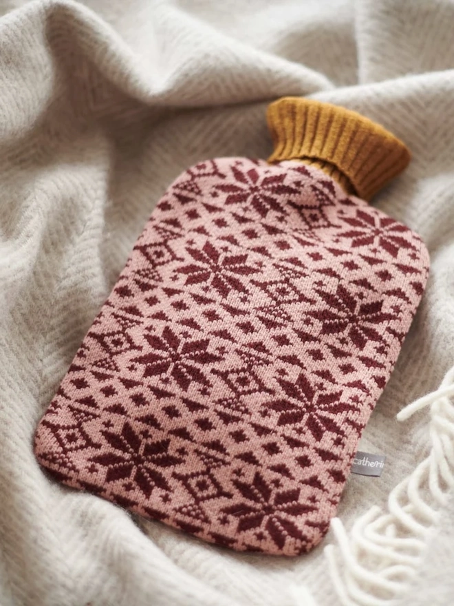 Lambswool Hot Water Bottle Cover, a colourful hot water bottle cover sitting on a blanket. 