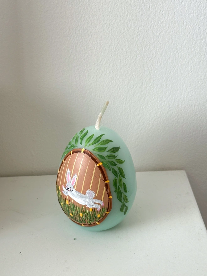 Hand Painted Easter Egg Candle Bunny, an Easter egg candle sitting on a plain surface. It's Easter and floral design wraps around it. 