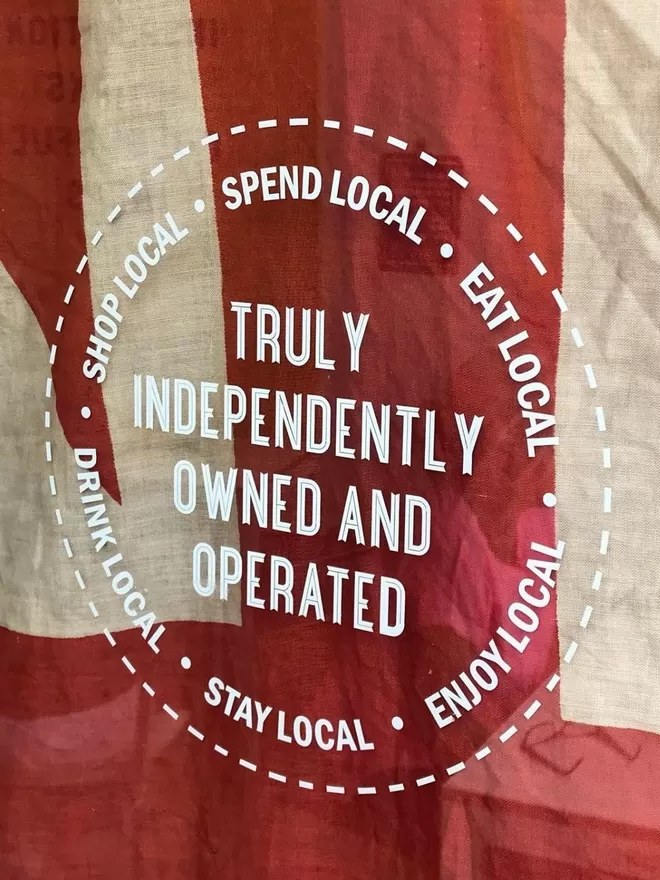 Independently owned sticker designed by Holly and Co see in a shop window with a flag behind.