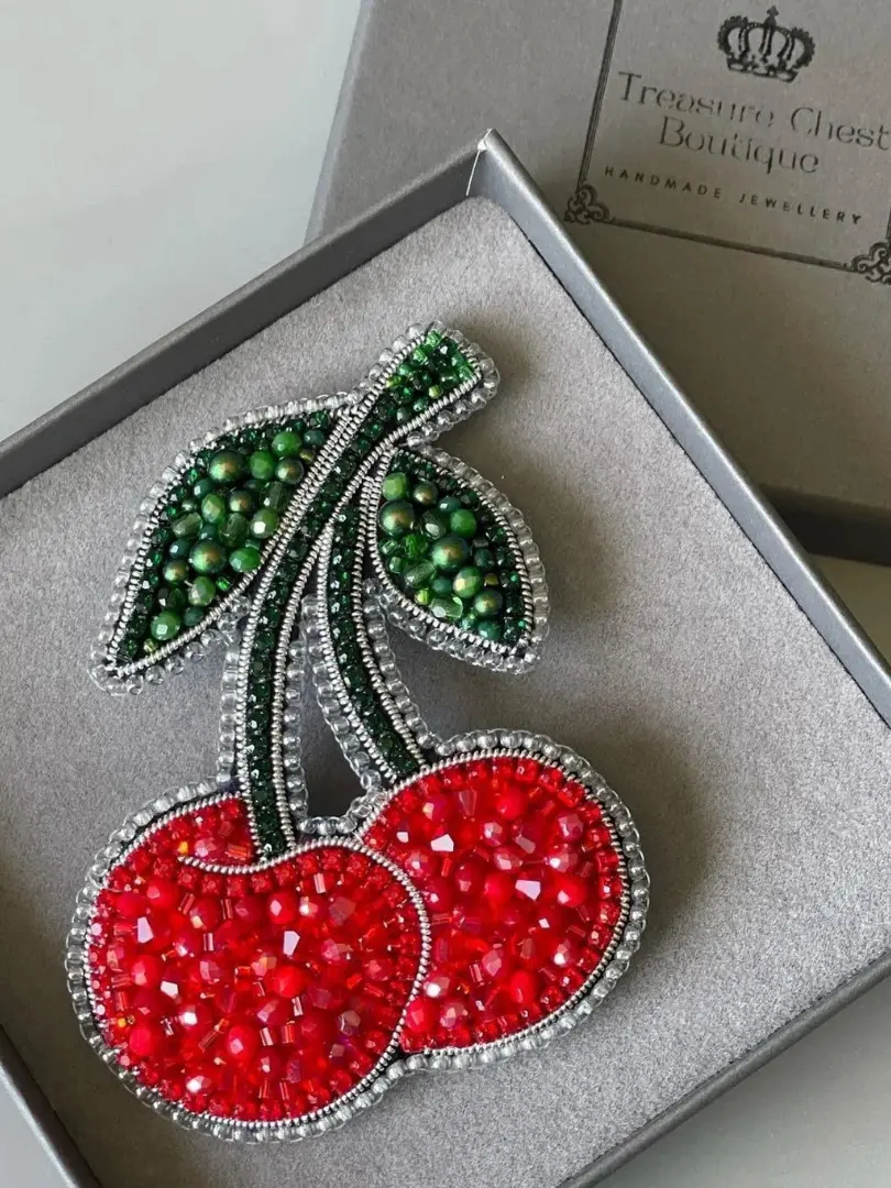 Red Cherry Beaded Brooch displayed in a grey gift box, on top of a grey table. 