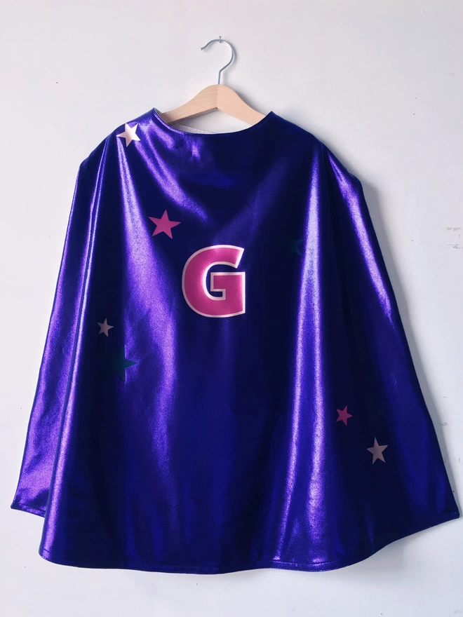 Purple superhero cape with pastel pink lining, large G initial in magenta and pastel pink, star cluster design