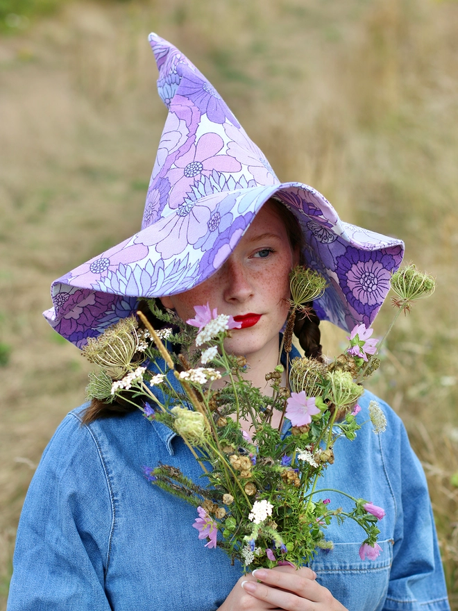 Young lady in field with flowers wearing upcycled fabric witch hat