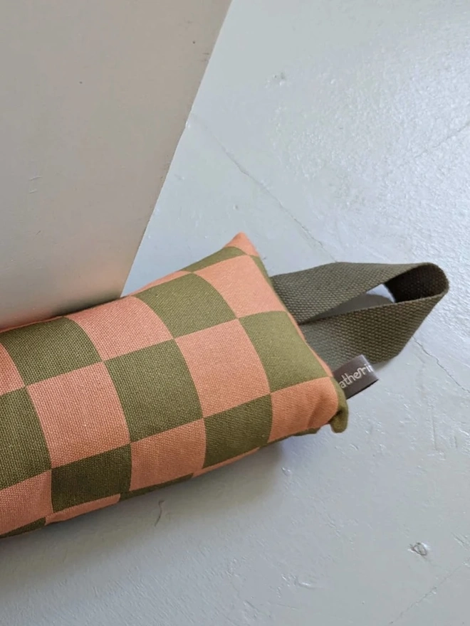 Draught Excluder, a colourful patterned draught excluder sitting on the floor by a white door. 