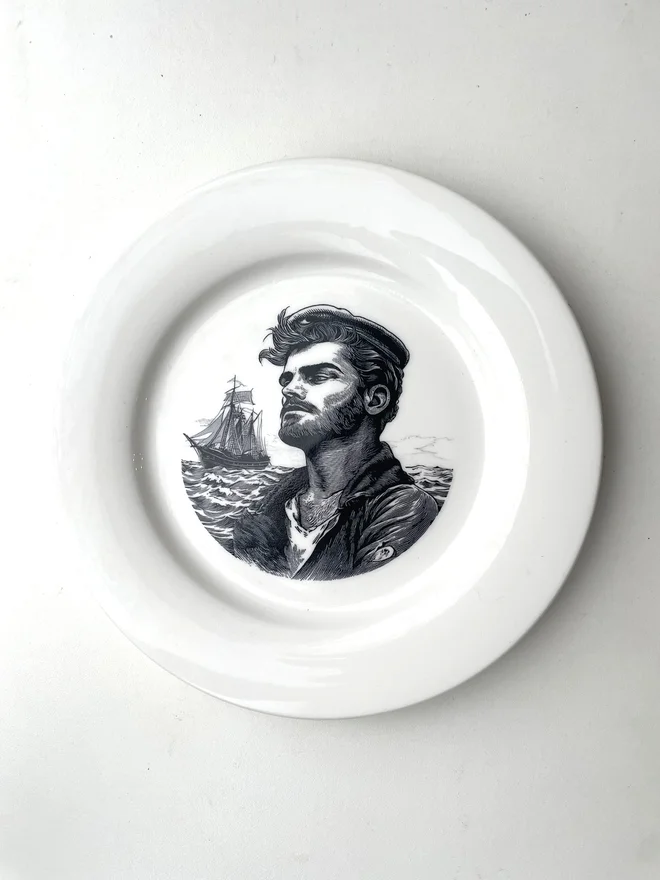 a white plate with a printed vintage illustration of a sailor man in the middle with the ocean and his ship behind him