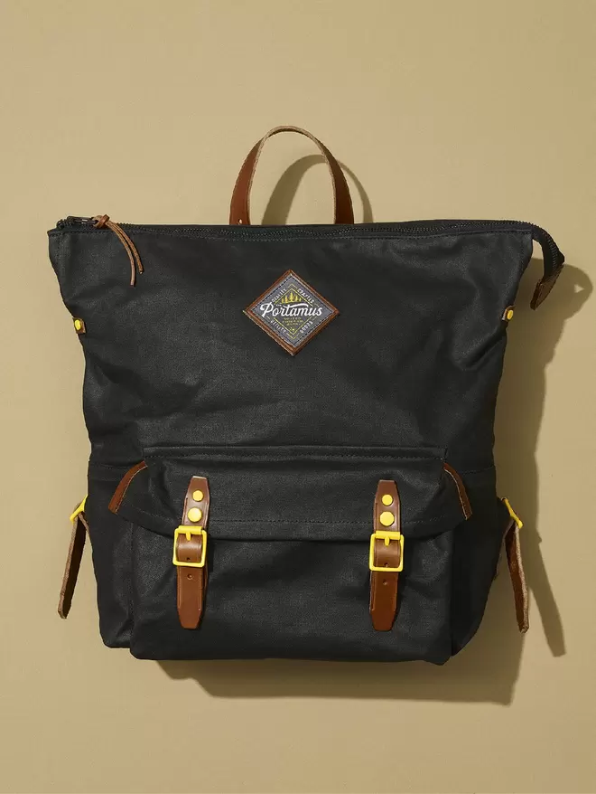 Black wax cotton zip top Shortwood backpack with brown leather trim and yellow hardware.