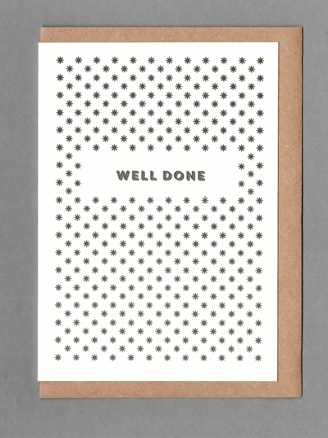 White card with black stars and black text reading 'WELL DONE' with a kraft envelope behind it