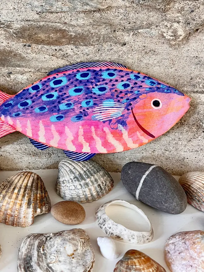 large wooden fish wall decoration. wooden fish decoration laid on wooden surface with seashells and pebbles.