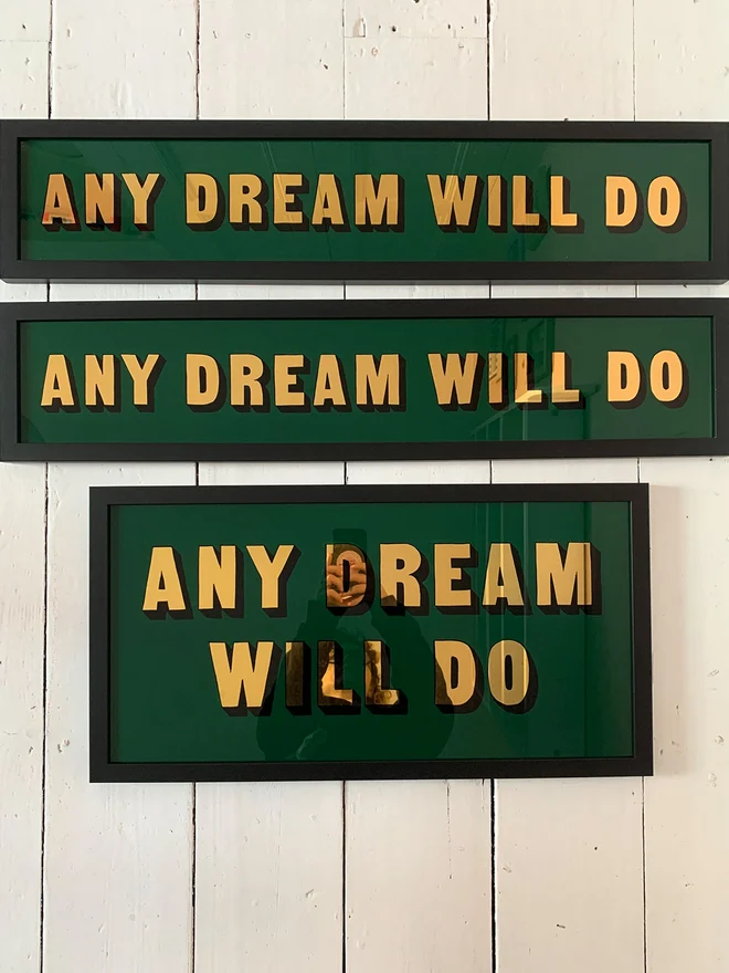 Three Any Dream Will Do Signs, all with a dark green background and with a black frame. The photo was taken on white floorboards