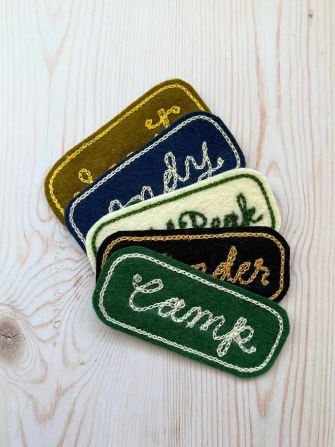 Five custom chain stitch embroidered patches laying on a wooden background in various colours
