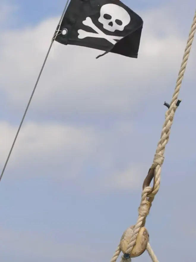 a black pennant flag with an ivory skull and crossbone on flying from a boat mast