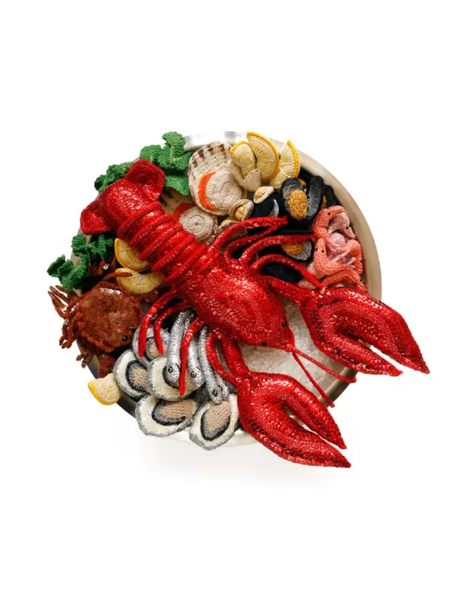 Image of Kate Jenkins' Fruits De Mer Print. The print is an image of Kate's crotched and embroidered sea fish and a large sequin lobster seen in a plate, against a white background.