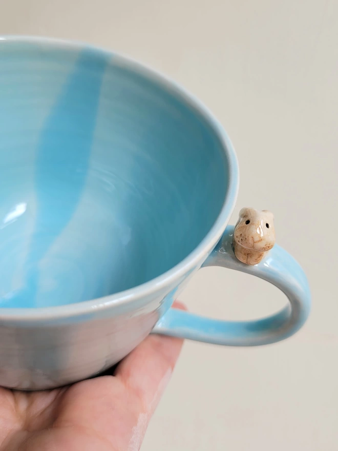 Pale turquoise blue ceramic cup with a cute beige bunny rabbit sitting on the side of the mug