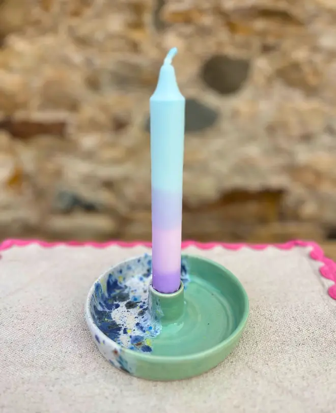 Shoreline Candle Stick Holder, a colourful candle stick holder sitting on a napkin, on a wooden surface against a brick backdrop. 