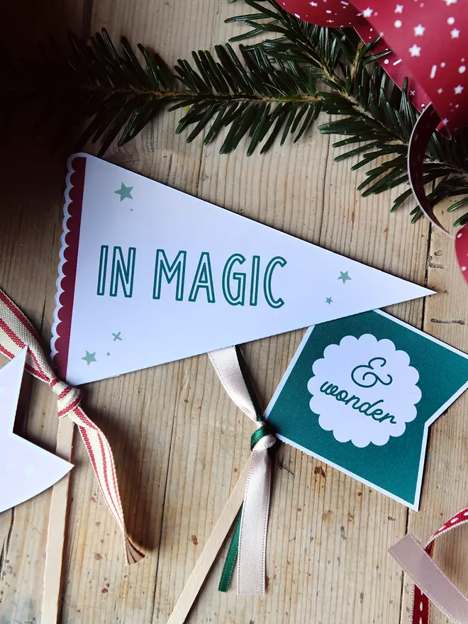 Two flags that read "in magic & wonder" lay on a wooden table beside festive greenery and a wrapped gift.