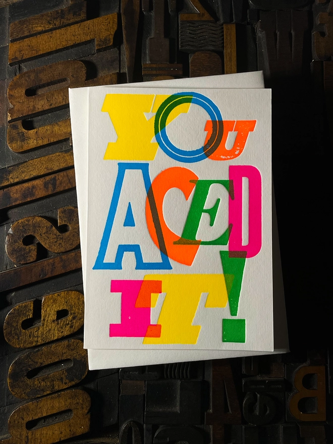 Colourful typographic letterpress card with bold overlapping neon letters spelling ‘You Aced It!’, perfect for celebrating exam success.
