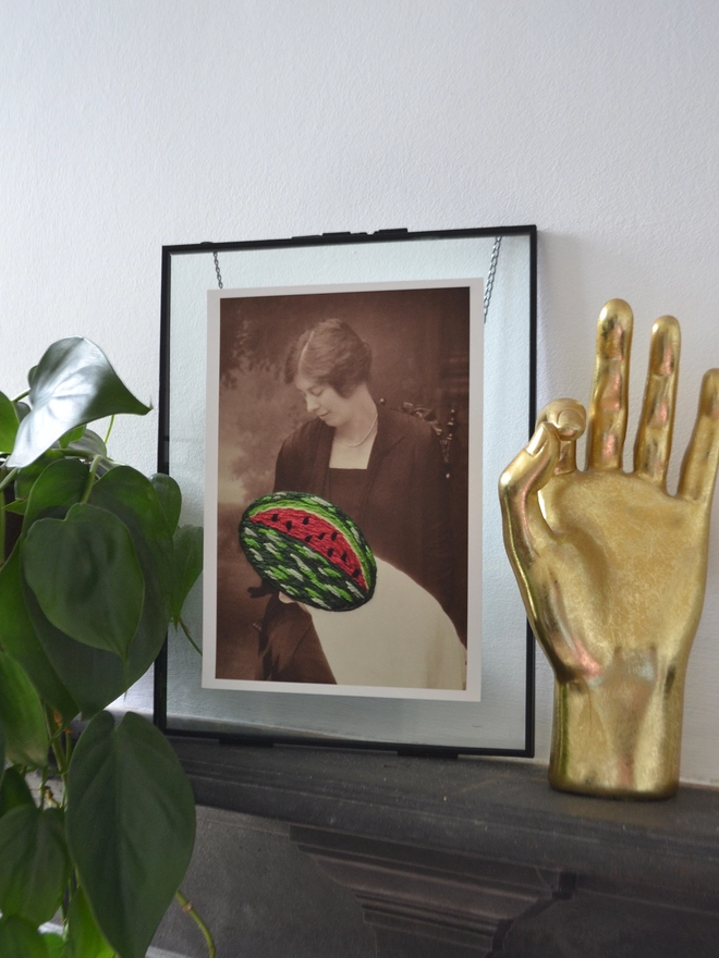 B&W photo print of woman holding embroidered watermelon framed on mantlepiece