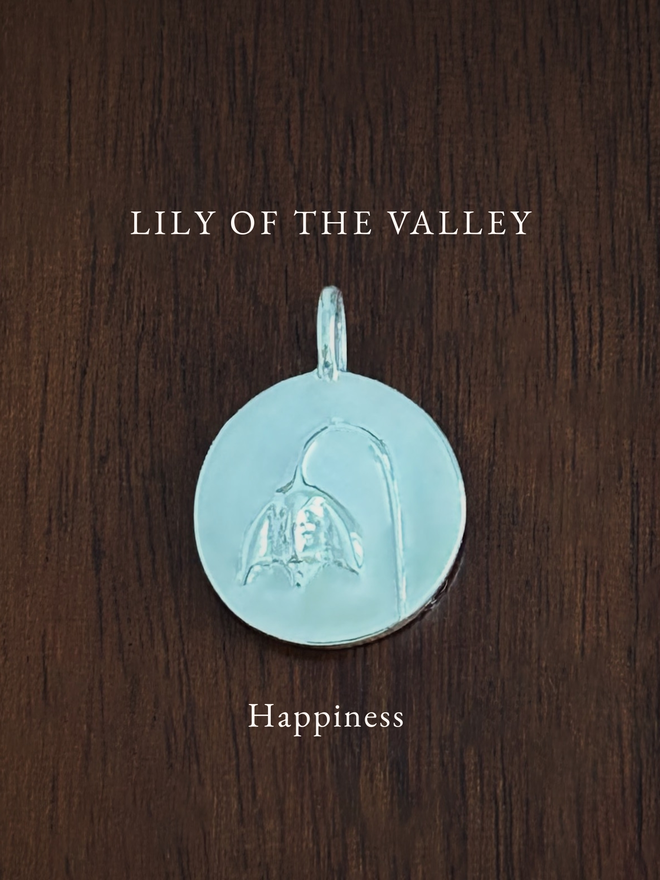 Sterling Silver Lily Of The Valley Coin Charm on a dark background with the language of flowers meaning, happiness
