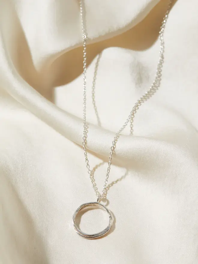 Dainty Sterling Silver Open Circle Necklace draped over silk material