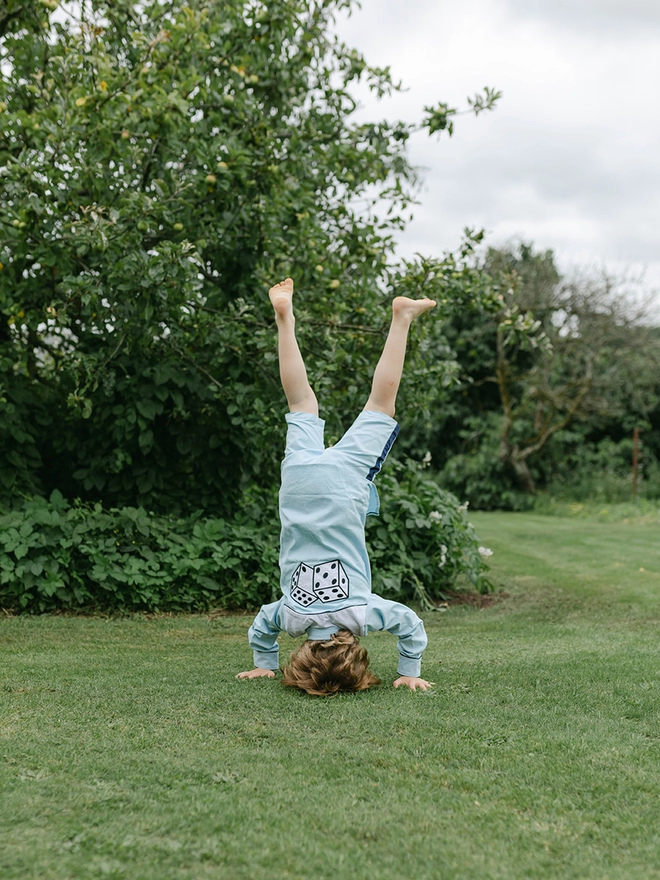 A boy in a blue cowboy shirt with dice appliqued on the back does a headstand in a garden