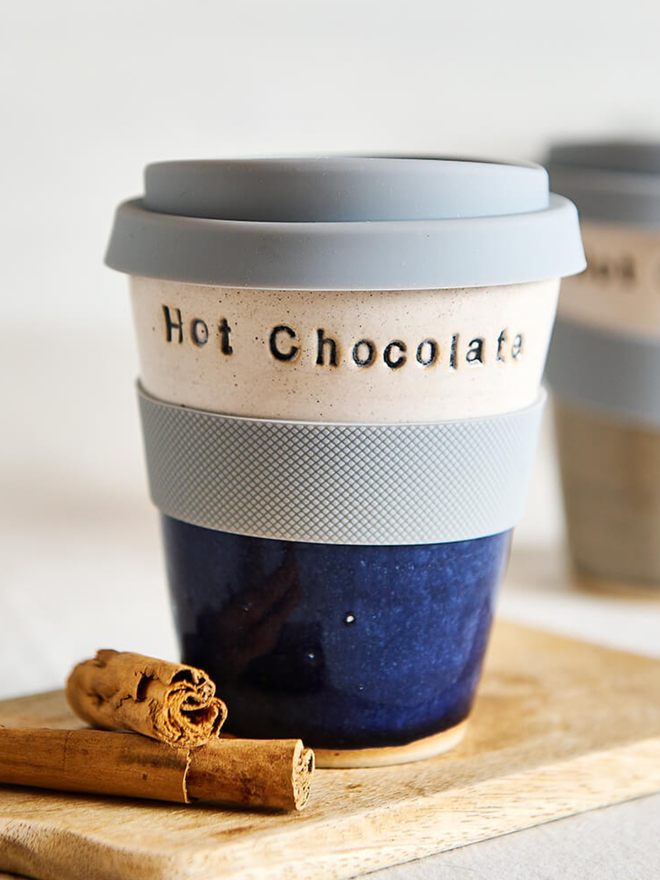 'hot toddy' ceramic travel mug. a dark blue and white travel mug, with light blue lid and band.