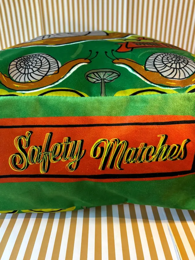 Snail Matchbox Cushion, a green decorated cushion sitting on a decorated surface. 