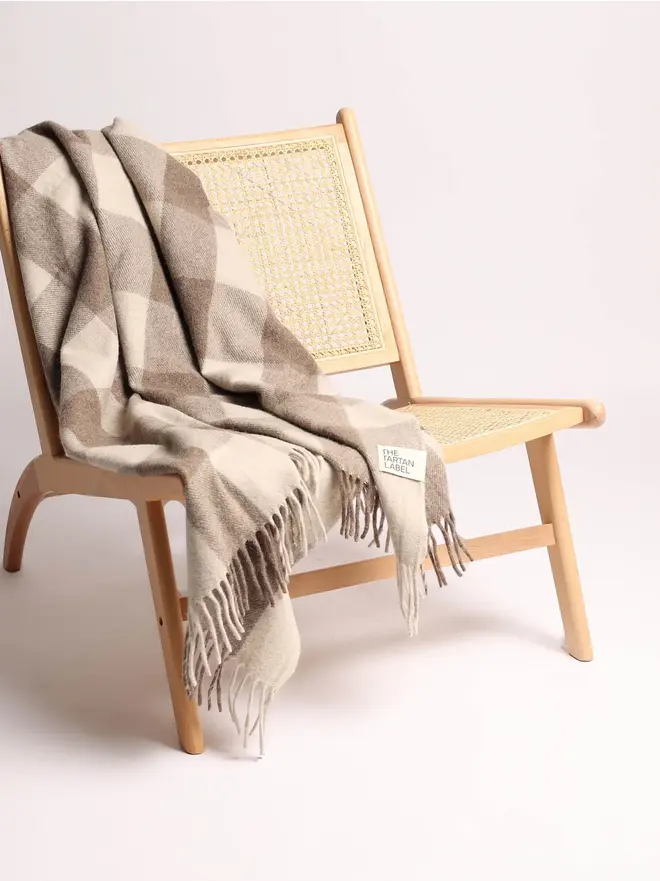 Jacob Blanket, a grey blanket draped over a wooden chair on a plain surface against a white backdrop. 