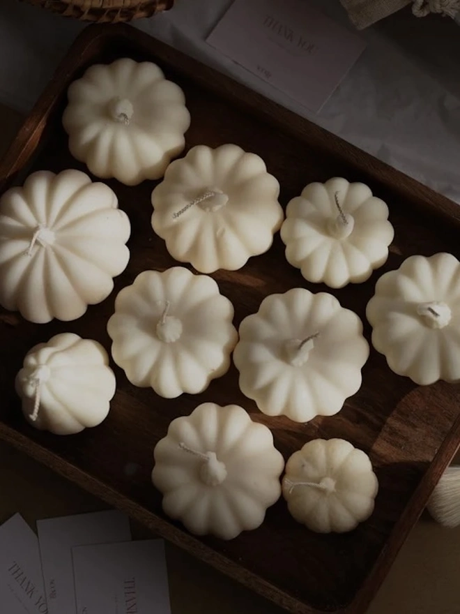 Medium Natural Wax Pumpkin. A collection of ivory pumpkin candles with braided wicks and sculpted stalks, arranged on a dark wooden tray in warm sunlight. The handmade candles make thoughtful autumn gifts or wedding and party favours.