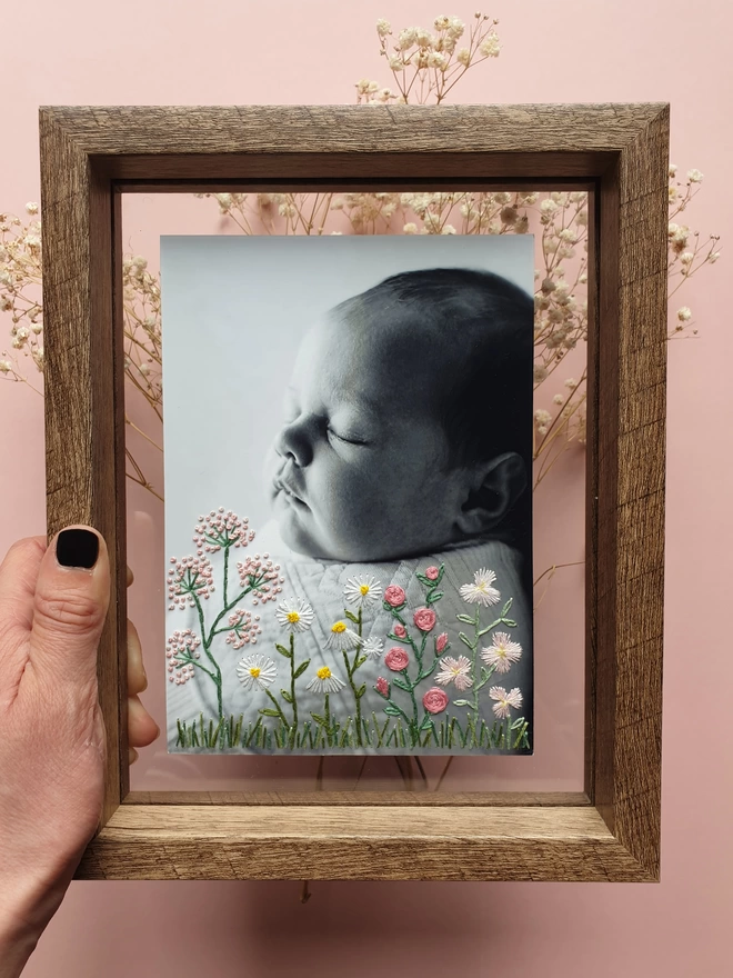 Baby photo with hand embroidered flowers growing from bottom of image, held in double glass frame
