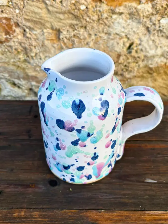 Sweetpea Medium Jug, a colourful jug placed on a wooden surface against a brick backdrop. 