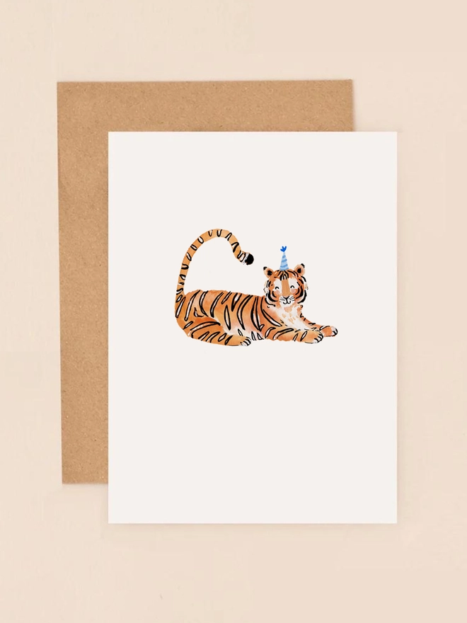 A playful illustration of a cheerful tiger lounging on its belly, wearing a festive blue party hat adorned with a pom-pom. The tiger's orange and black stripes are depicted in soft, flowing lines, adding to its friendly expression. The card's minimalist design features a neutral background, allowing the tiger and its party hat to take center stage.