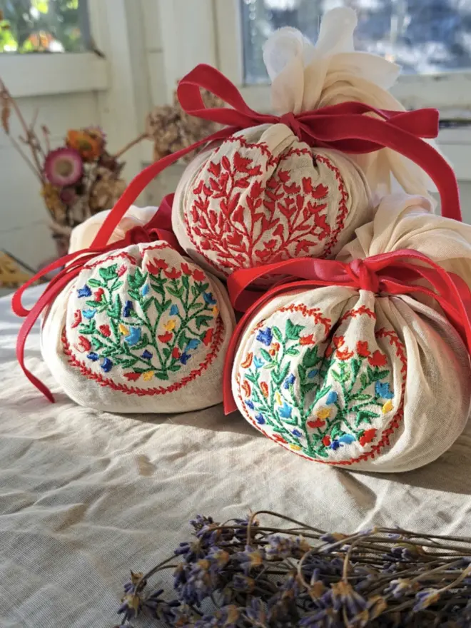 stack of three linen sacks, with floral embroidery and red ribbon ties