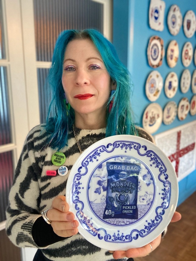 Lucy holding an 8" blue and white 'Delft' style plate featuring a packet of Monster Munch