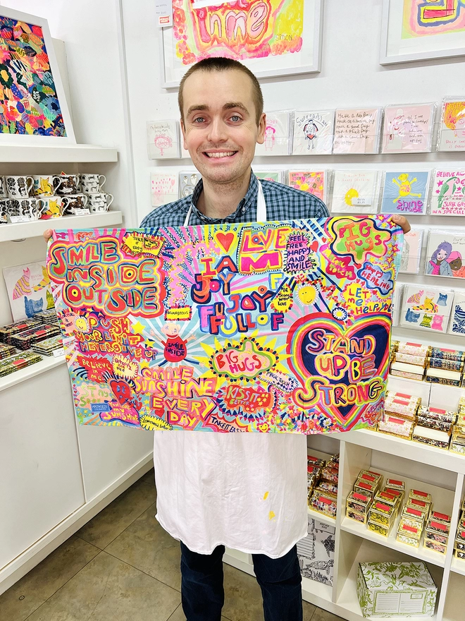 Happy artist holding full of joy 100% organic cotton charity tea towel with colourful positive messages