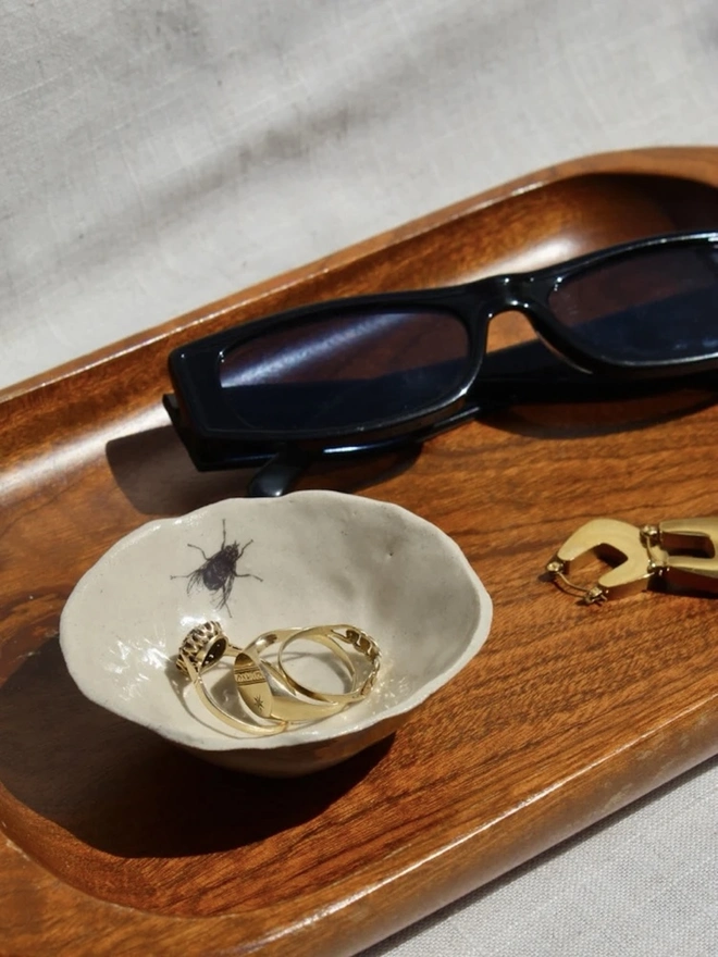 Fly Trinket Dish, a fly trinket dish sitting on a wooden surface joined by other accessories. 