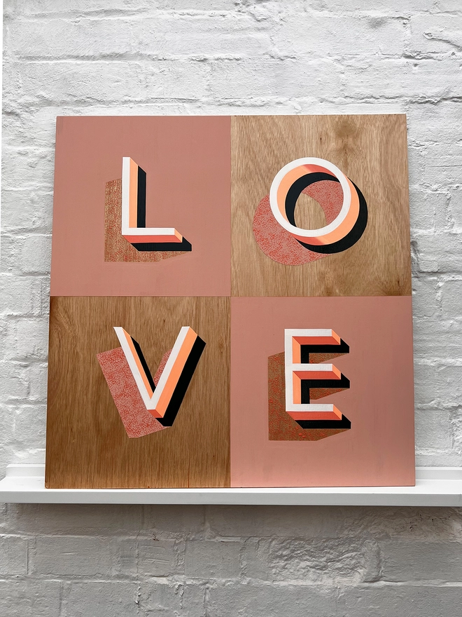 LOVE hand painted sign in pinks and neon orange, against a white brick wall, straight on. 