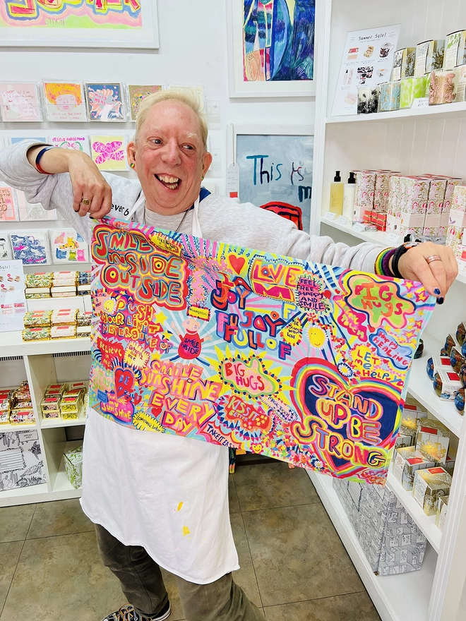 Happy artist holding full of joy 100% organic cotton charity tea towel with colourful positive messages