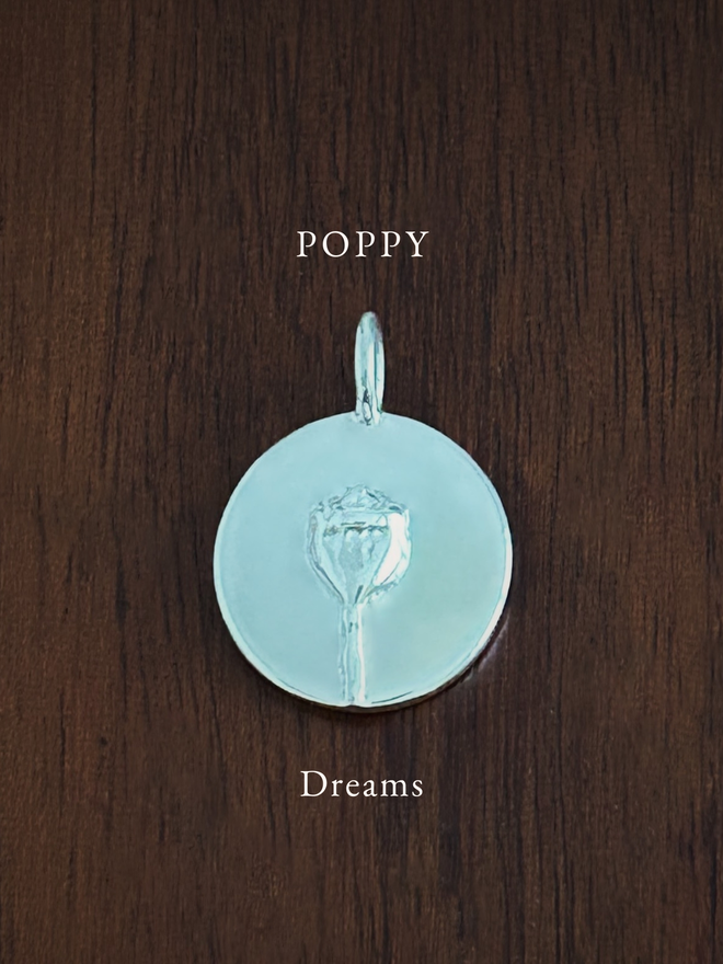 Sterling Silver Poppy Coin Charm on a dark background with the language of flowers meaning, dreams