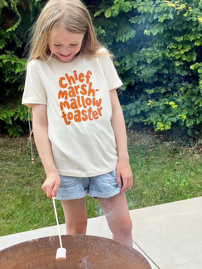 girl toasting marshmallows while wearing chief marshmallow toaster organic cotton kid's t-shirt 