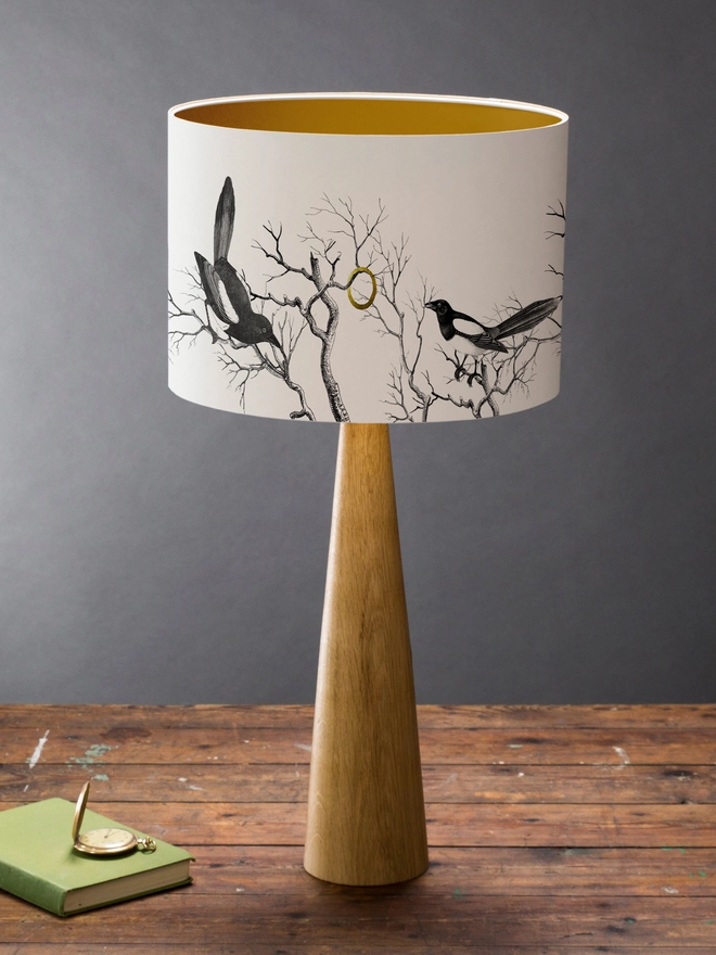Handmade lampshade featuring cheeky magpies with gleaming gold details, inspired by traditional folklore and whimsical home decor.