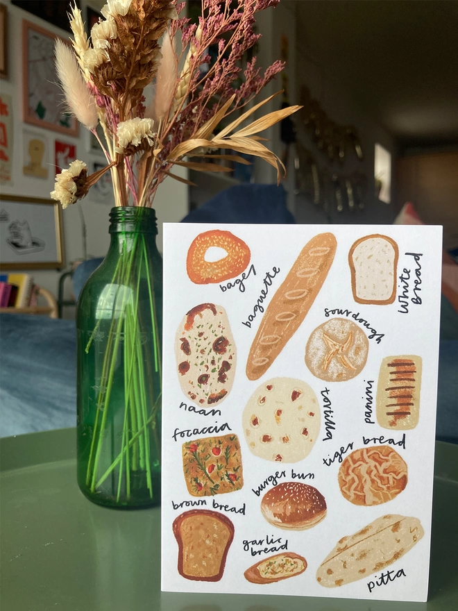 Greetings card illustrated with a selection of breads, placed on a table with flowers in the background.