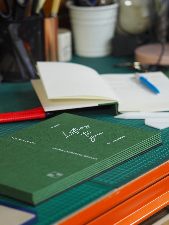 a workbench with a stack of green letters to your journal covers about to bound