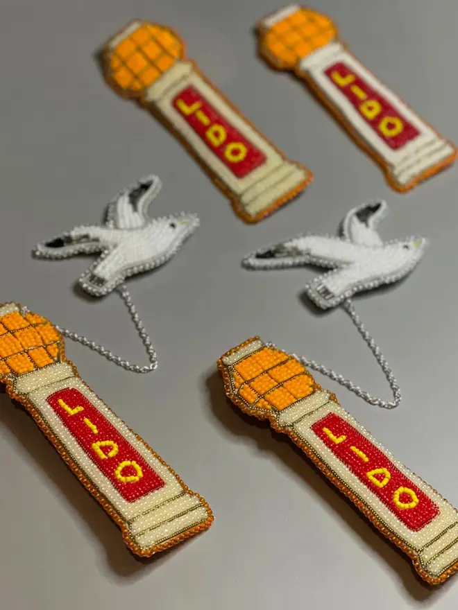 Beaded lido brooch with orange, red, and beige beads attached to a white beaded seagull by a silver chain, displayed on a grey table. 