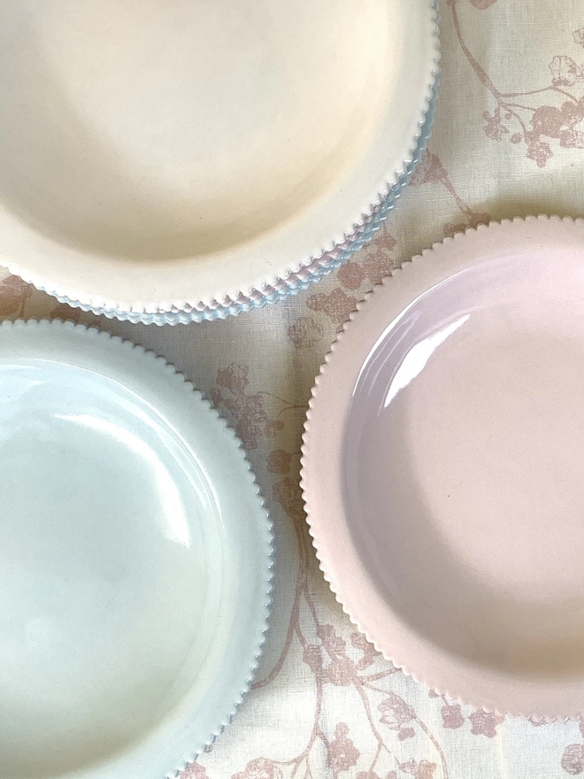 top view of scalloped edge pasta bowls in pale pink, white and soft blue